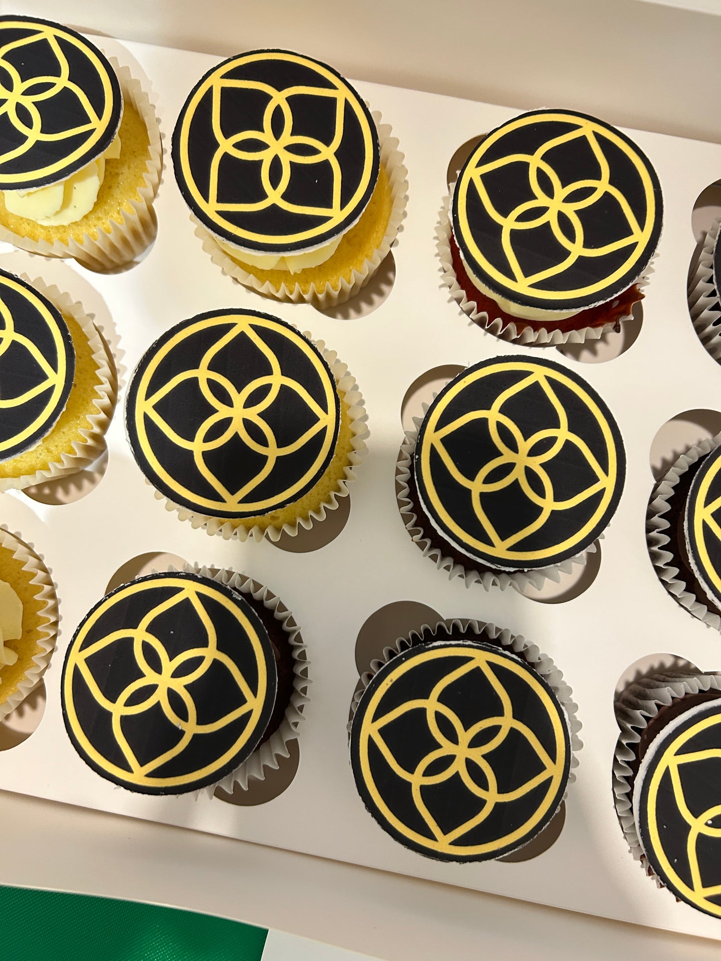 Cupcakes with logo in icing paper, black and gold designs on a white tray