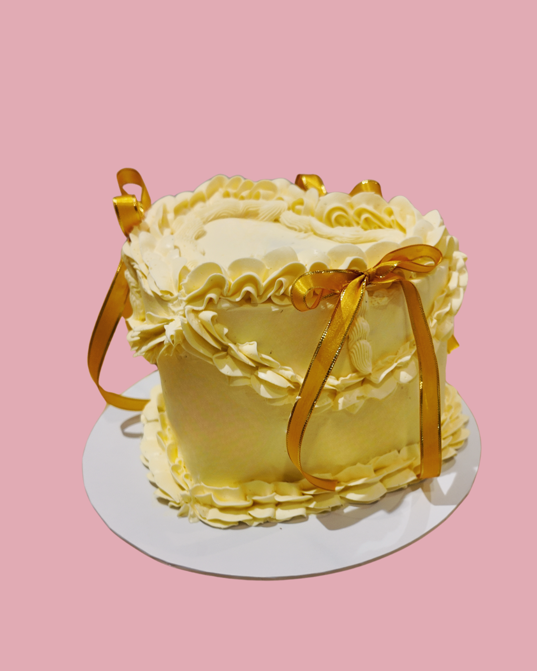 Heart Vintage cake.Yellow cake with ruffled details and gold ribbons on a pink background. 